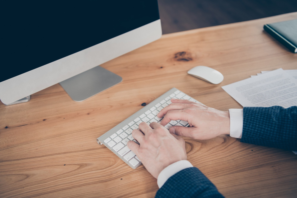 un rédacteur du clavier futé tapant sur un clavier blanc devant un écran d'ordinateur sur un bureau en bois