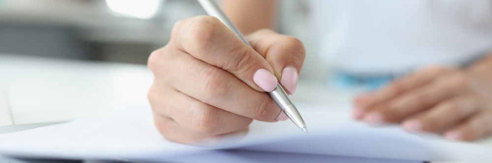 une main tenant un crayon à l'encre au-dessus d'une feuille blanche pour rédiger un texte