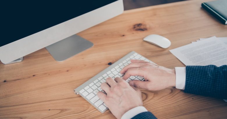 un rédacteur du clavier futé tapant sur un clavier blanc devant un écran d'ordinateur sur un bureau en bois